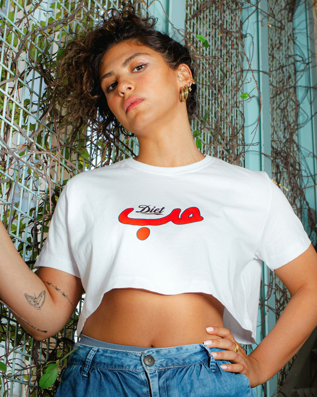 Young adult female wearing white Crop Top with Diet Hobb written in English and Arabic حب and printed in red silkscreen in the center of the Crop Top.