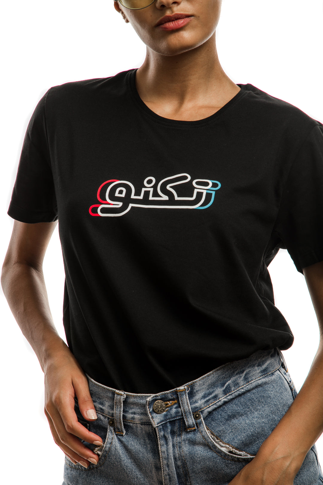 Young adult female wearing black T-shirt with Techno written in Arabic تكنو and printed in blue, red and white silkscreen in the center of the t-shirt along with blue jeans shorts.