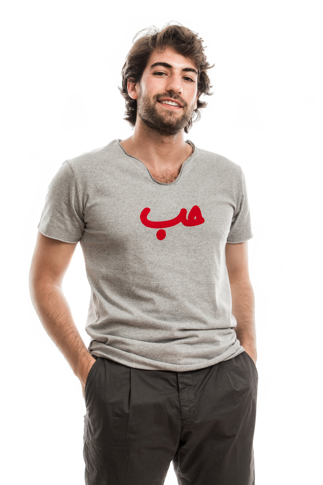 Young adult male wearing grey T-shirt with Hobb written in Arabic حب and printed in red velvet in the center of the T-shirt along with black pants.