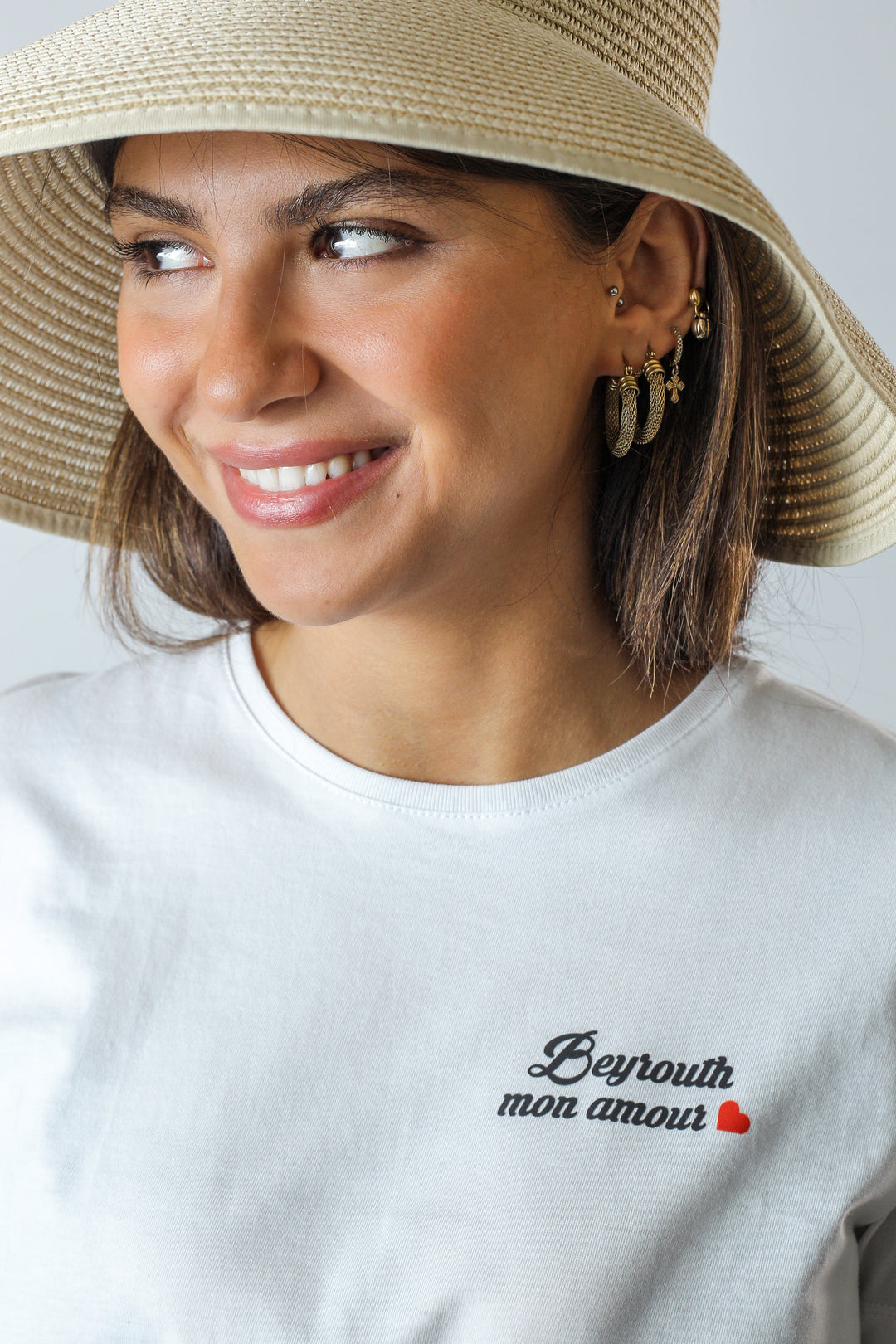 Young adult female wearing a white T-Shirt with Beyrouth mon amour written in French and printed in silkscreen along with a beige hat.