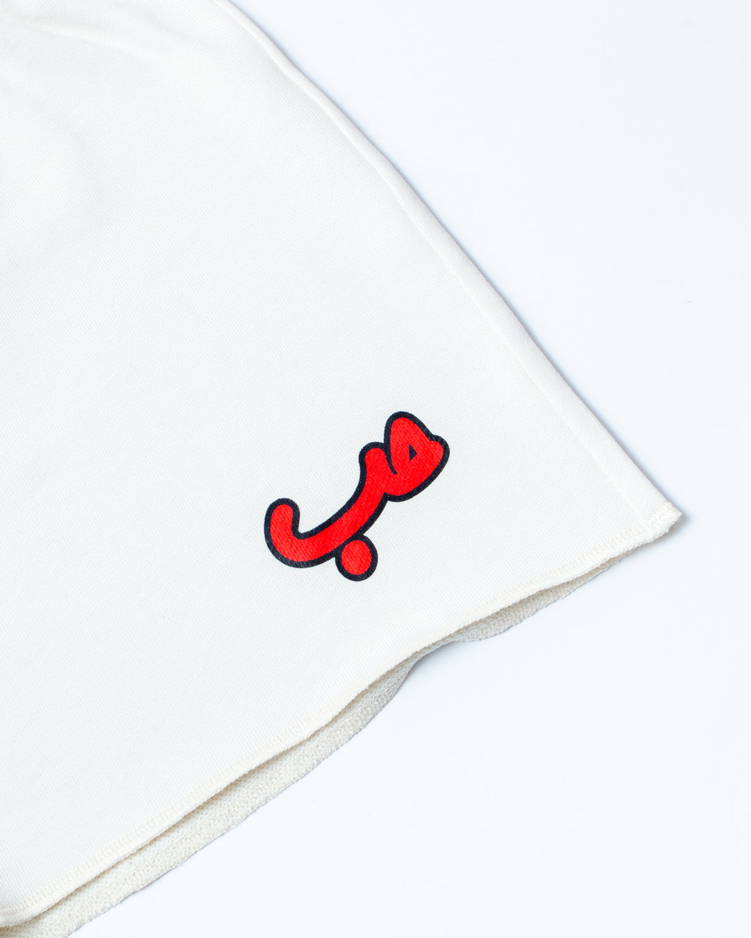 Close up on Hobb written in Arabic حب and printed in red silkscreen on the side of a flared off white short.