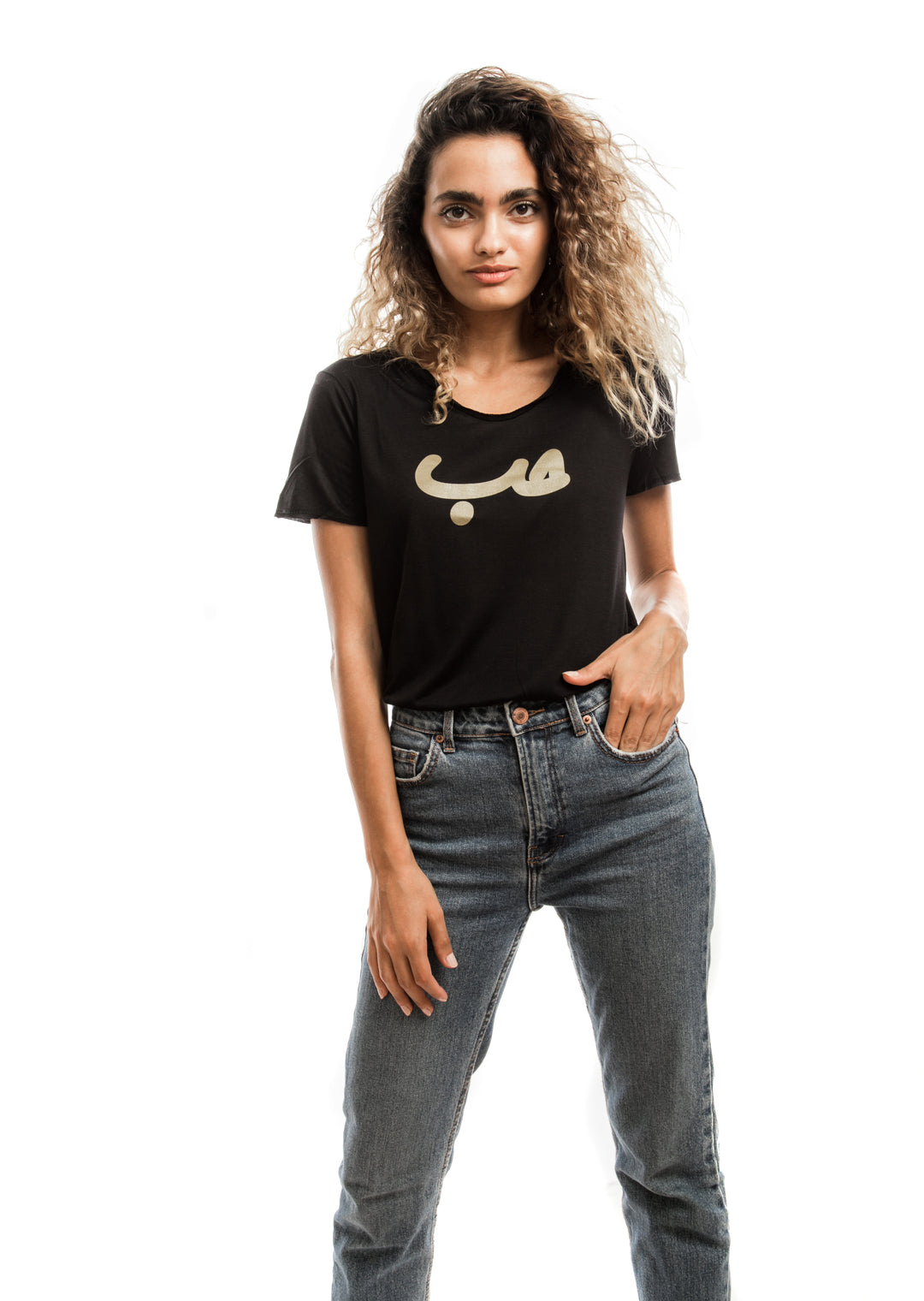Young adult female wearing black T-shirt with Hobb written in Arabic حب and printed in gold silkscreen in the center of the T-shirt along with jeans.