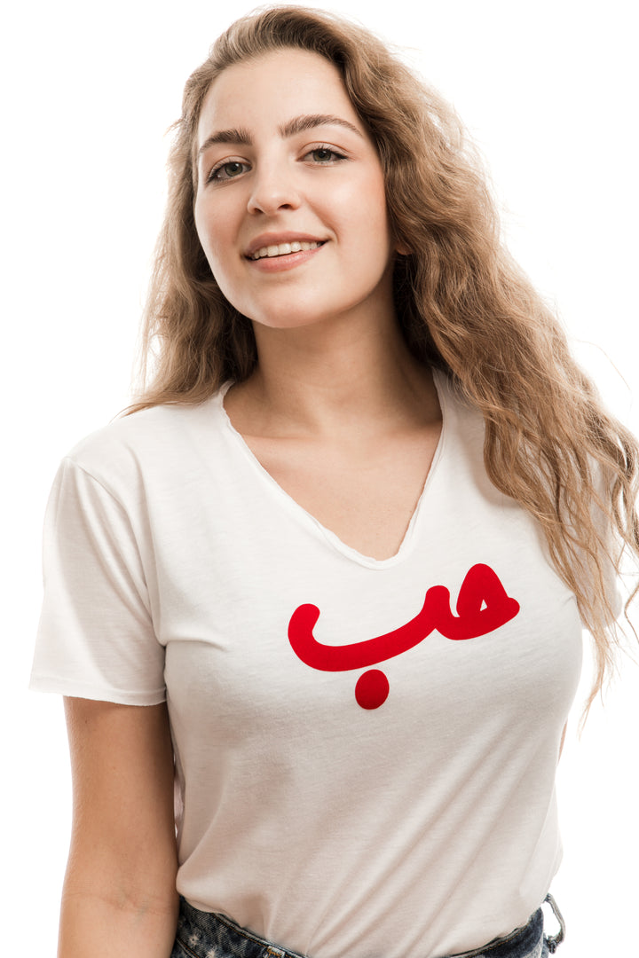 Young adult female wearing white T-shirt with Hobb written in Arabic حب and printed in red velvet in the center of the T-shirt.
