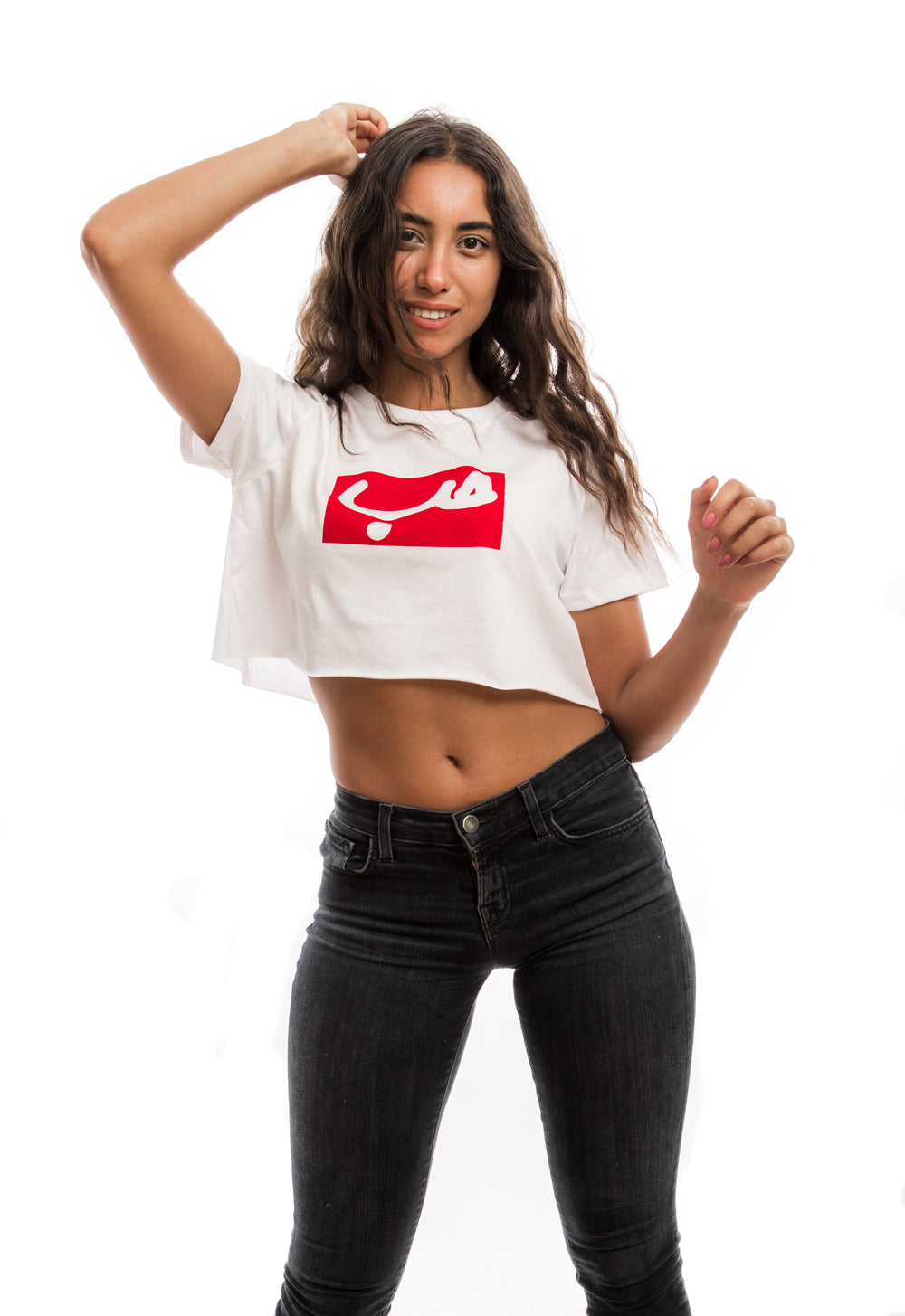 Young adult female wearing white Crop Top with Hobb written in Arabic حب in white and printed in a red velvet frame in the center of the Crop Top along with black jeans.