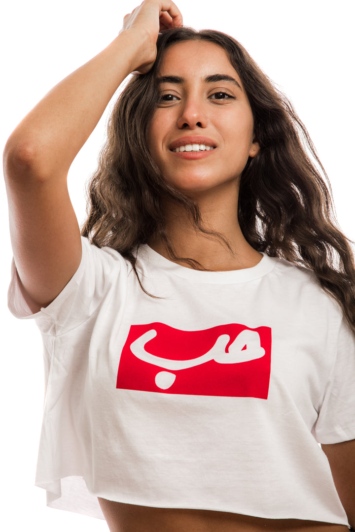 Young adult female wearing white Crop Top with Hobb written in Arabic حب in white and printed in a red velvet frame in the center of the Crop Top.
