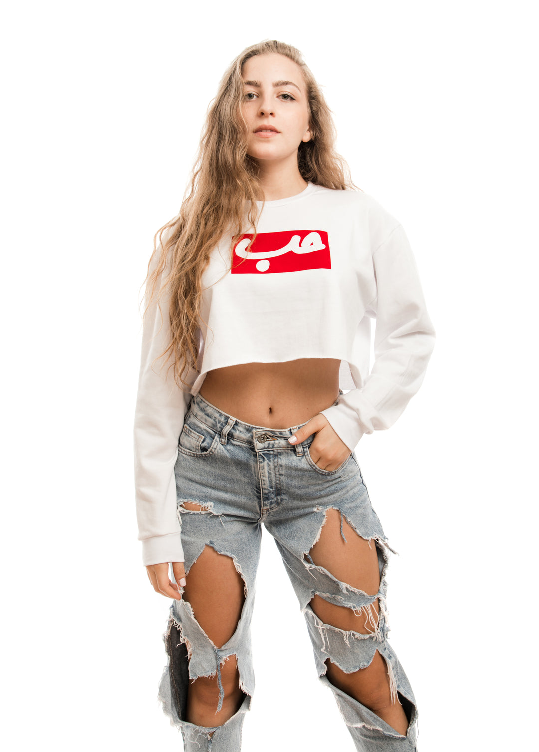 Young adult female wearing white Crop Sweater with Hobb written in Arabic حب in white and printed in a red velvet frame in the center of the Crop Sweater along with teared jeans.