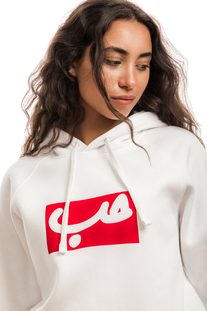 Young adult female wearing white Hoodie with Hobb written in Arabic حب in white and printed in a red velvet frame in the center of the Hoodie.